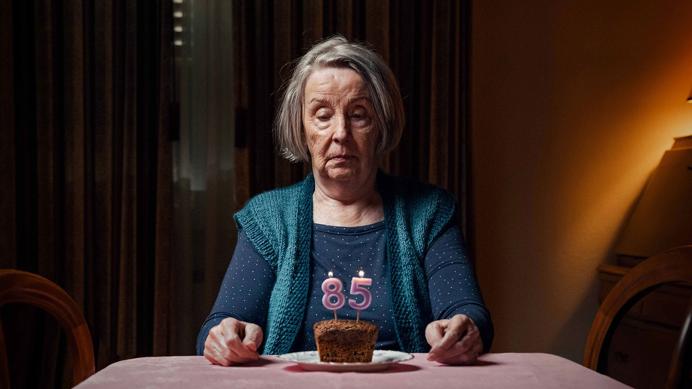 Une personne âgée est assise devant un gâteau d'anniversaire