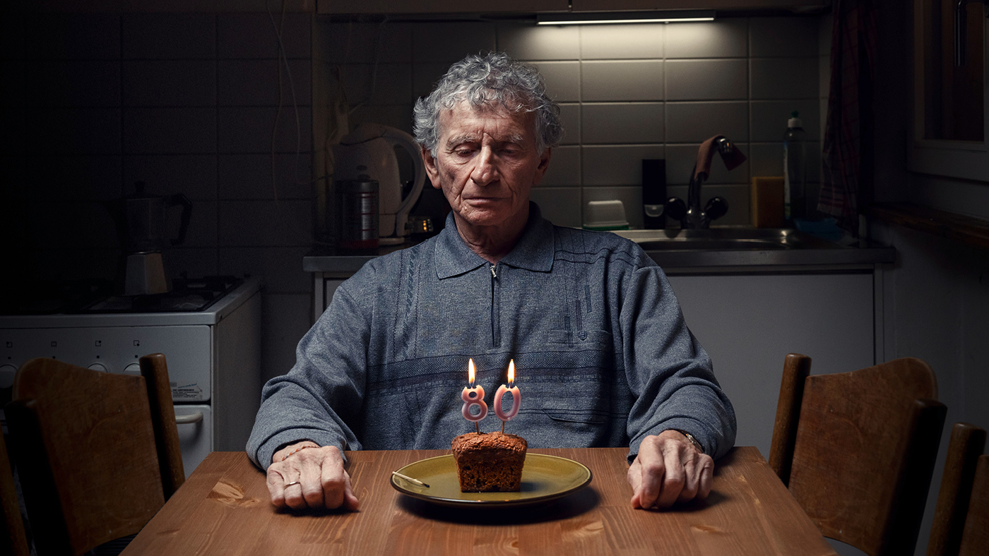 Un'anziana signora siede da sola davanti a una piccola torta di compleanno. 