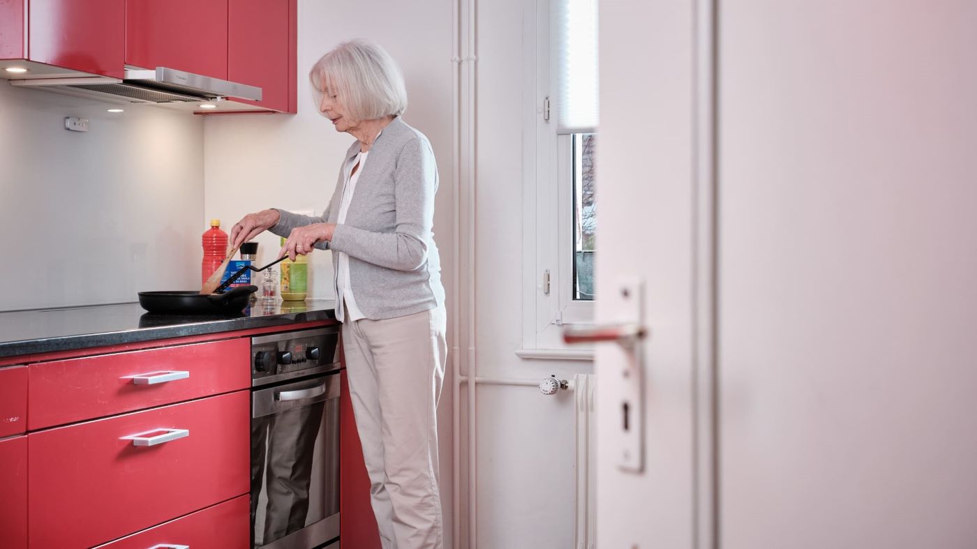 Eine ältere Frau steht in der Küche und kocht.